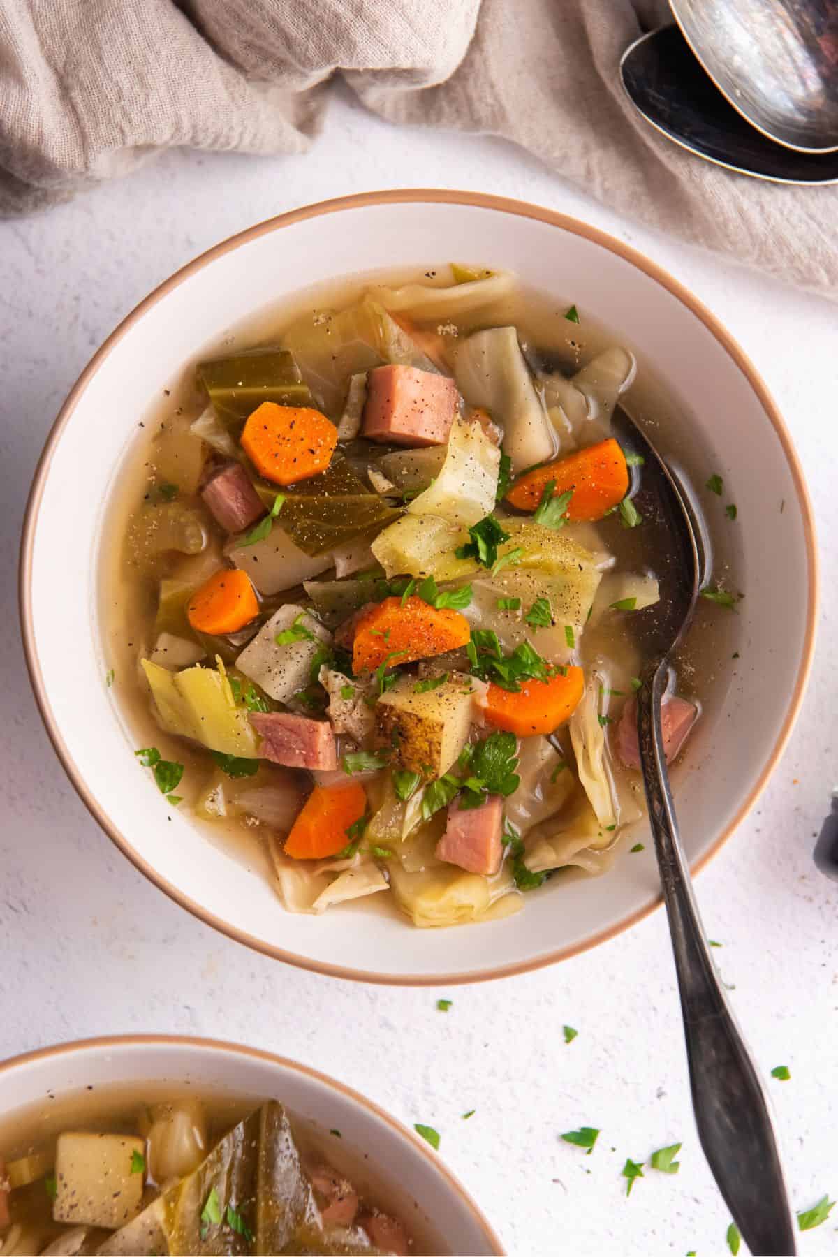 Overhead view of the ham and cabbage soup in a white bowl with a spoon.