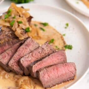 Slices of instant pot steak on plate with creamy sauce drizzle