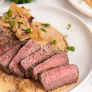 Slices of instant pot steak on plate with creamy sauce drizzle
