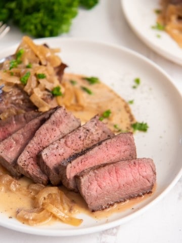 Slices of instant pot steak on plate with creamy sauce drizzle