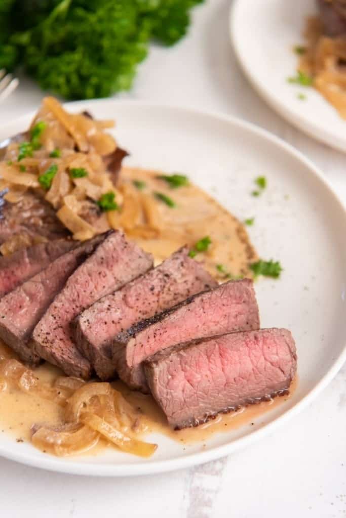 Slices of instant pot steak on plate with creamy sauce drizzle