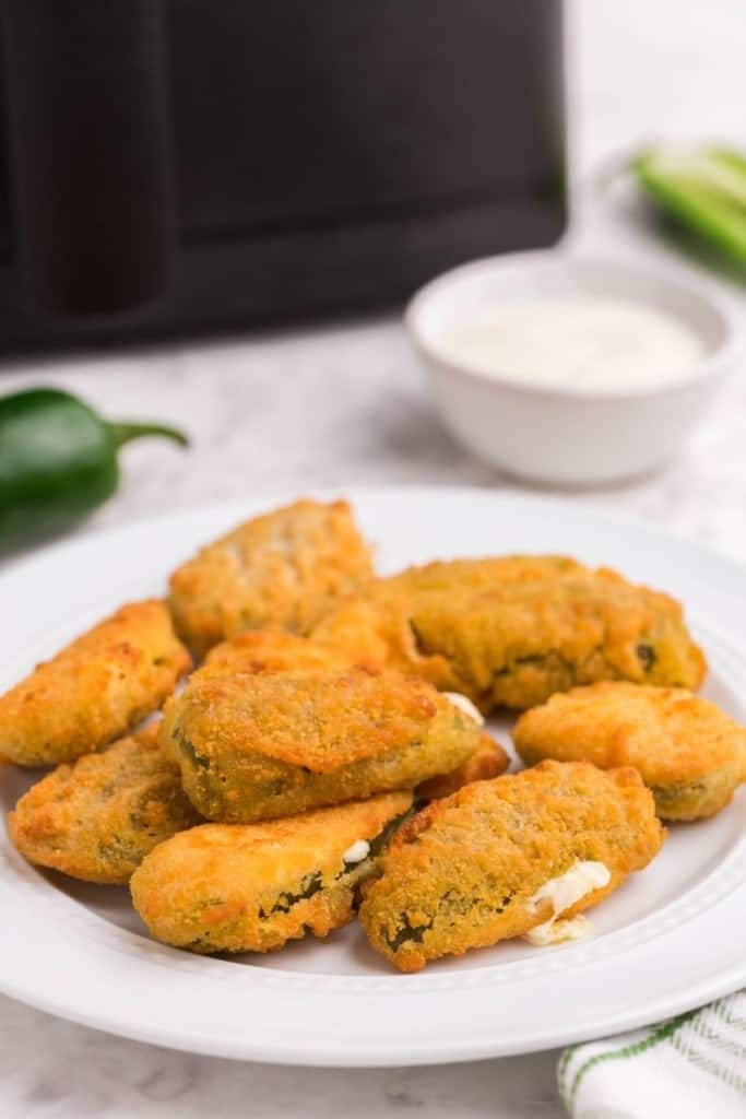 pile of jalapeno poppers on white plate with dipping sauce 