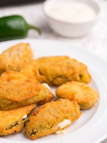 Golden jalapeno poppers on plate with dipping sauce on the side