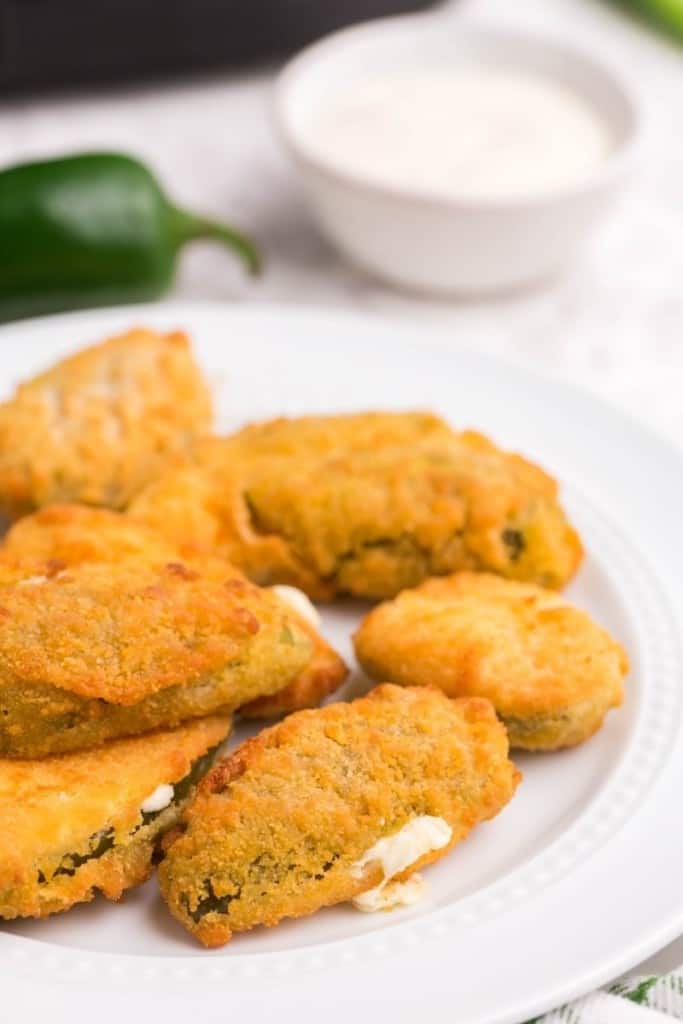 Golden jalapeno poppers on plate with dipping sauce on the side
