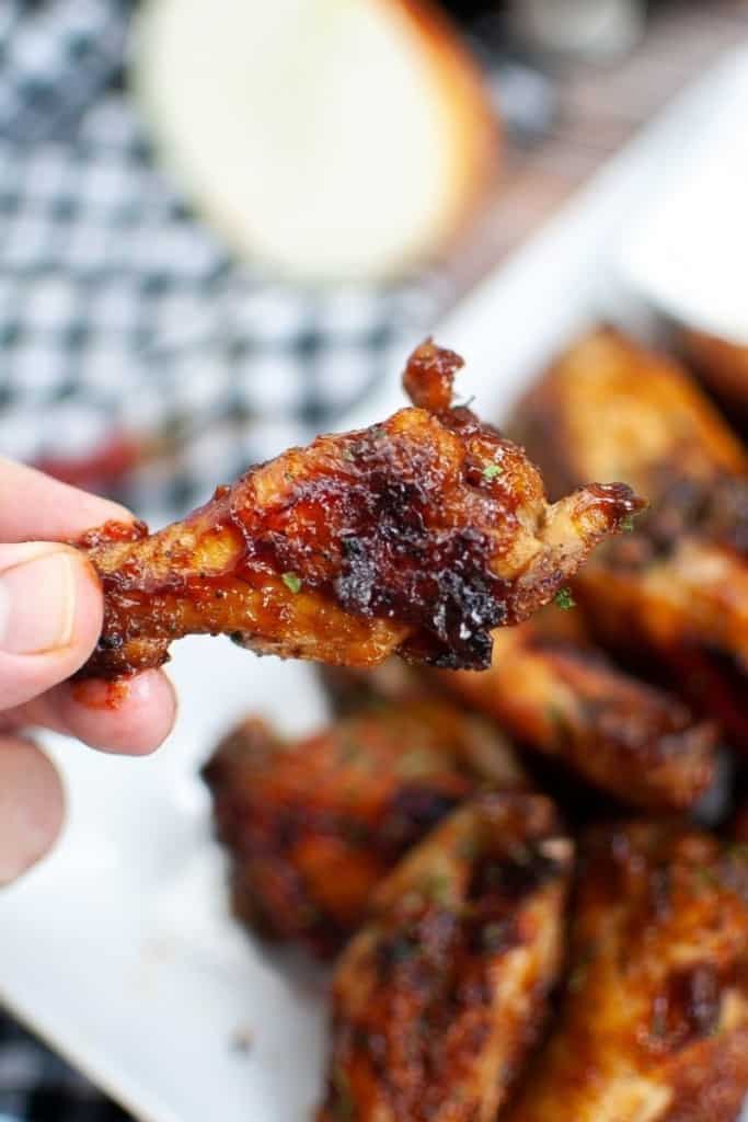 Piece of air fryer bbq chicken wings held in hand over plate full