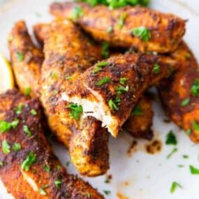 Chicken tenders without breading cooked in air fryer on plate with a bit taken out of one