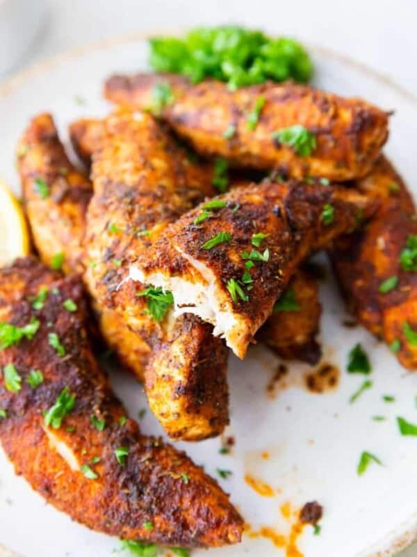Chicken tenders without breading cooked in air fryer on plate with a bit taken out of one