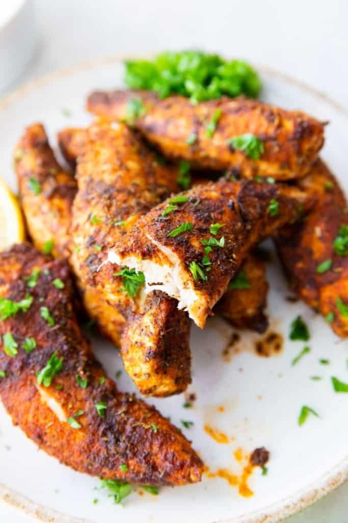 Chicken tenders without breading cooked in air fryer on plate with a bit taken out of one