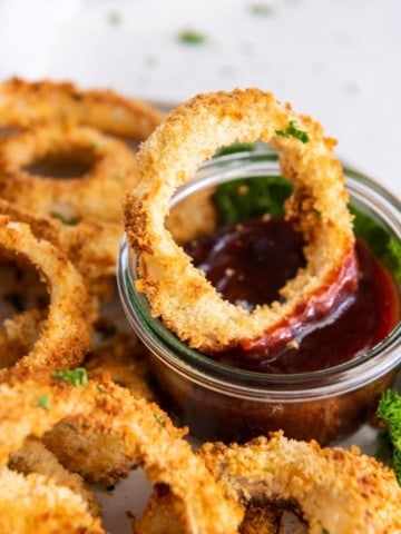 Crispy homemade air fryer onion rings on plate in dipping sauce