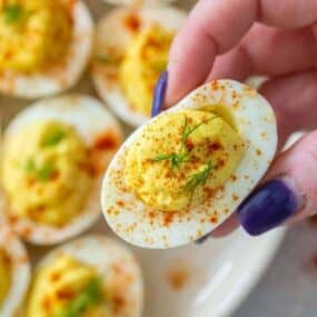 Hand grabbing a deviled egg without vinegar from plate
