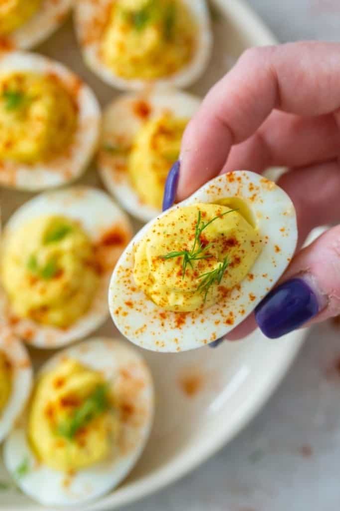 Hand grabbing a deviled egg without vinegar from plate