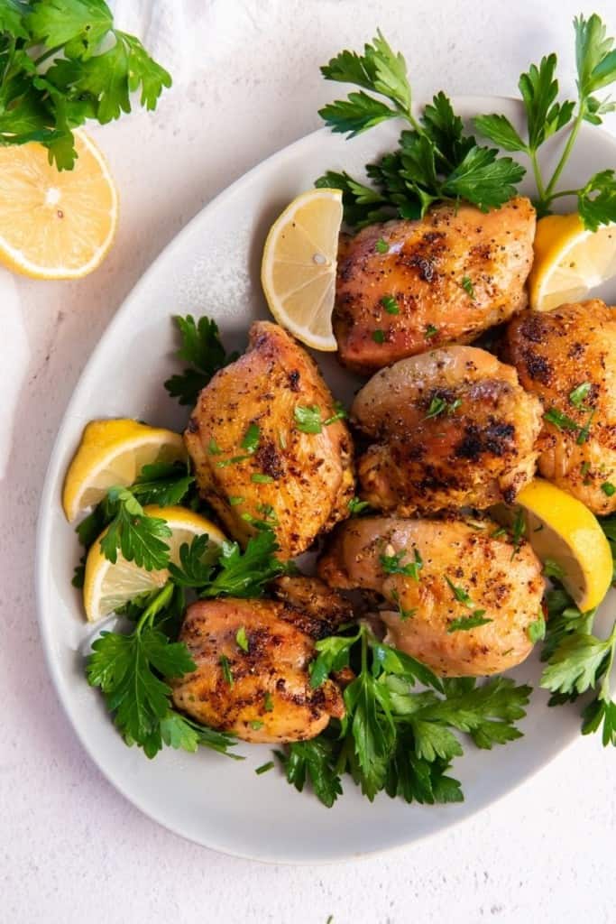 seasoned chicken thighs on plate with greens and lemon wedges