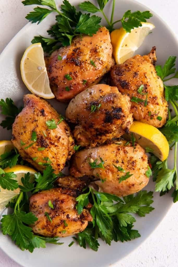 chicken thighs on plate with greens and lemon wedges