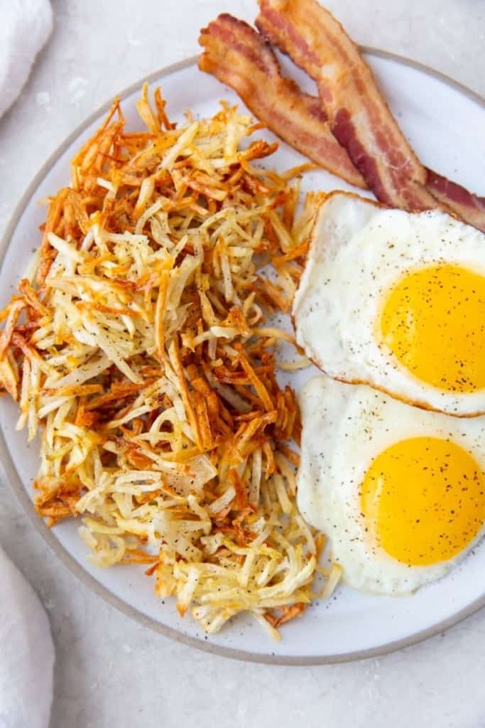 air fryer hash browns on plate with bacon and fried eggs