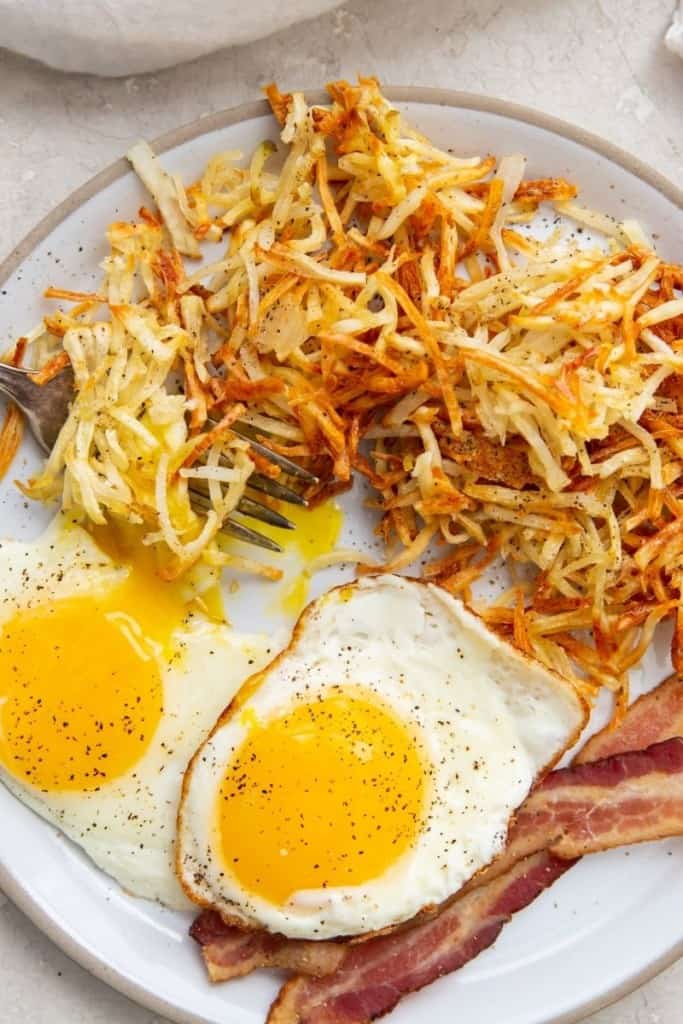 air fryer hash browns on plate with bacon and fried eggs