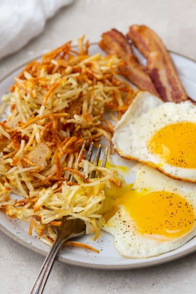 Crispy hash browns cooked in the air fryer on plate with bacon and fried eggs