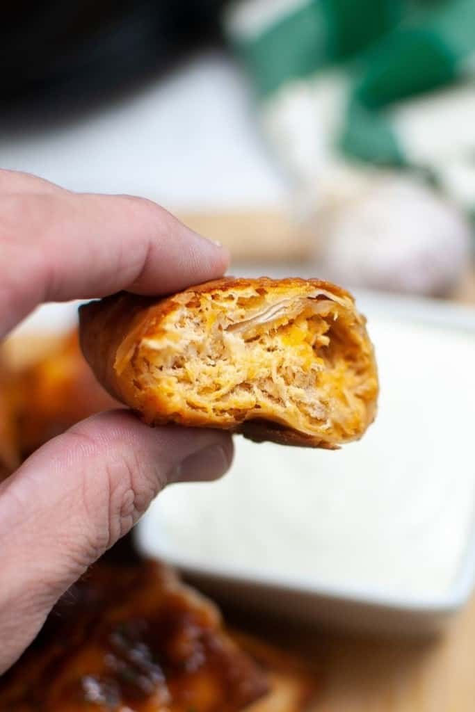 fingers holding bitten into buffalo chicken egg roll cooked in air fryer