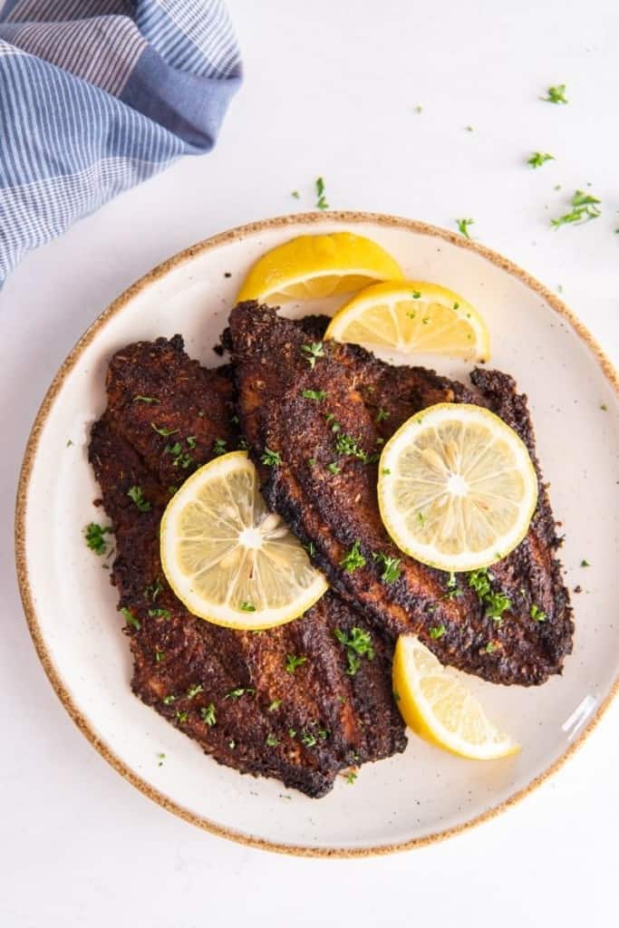 white plate with air fryer catfish fillets and lemon wedges