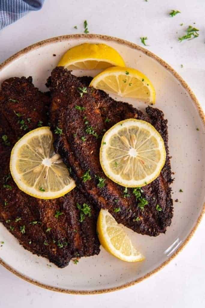 two air fryer catfish fillets on plate with lemon wedge garnish