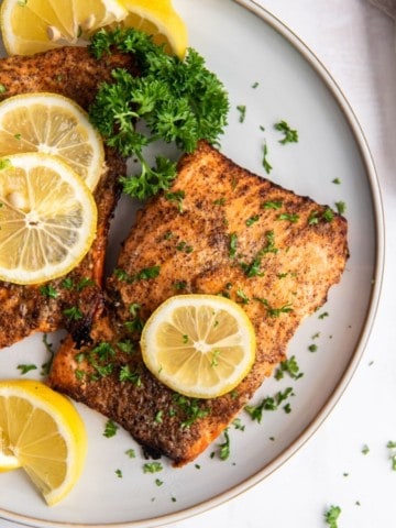 air fryer salmon fillets on white plate with lemon slices