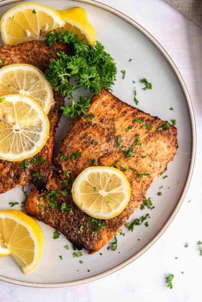 air fryer salmon fillets on white plate with lemon slices