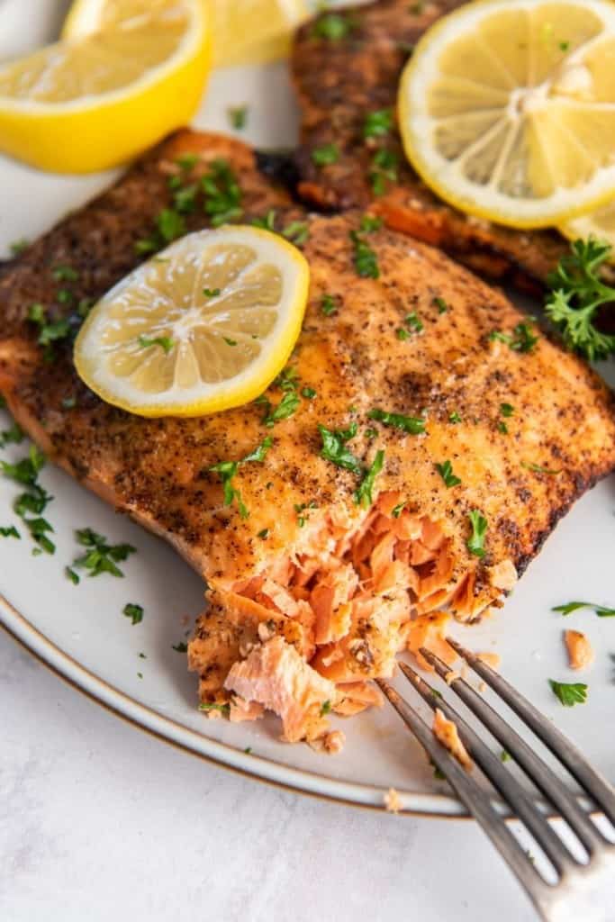 fork cutting piece of soft and flakey salmon fillet cooked in air fryer