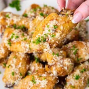 Hand reaching for one of many garlic parmesan wings on plate