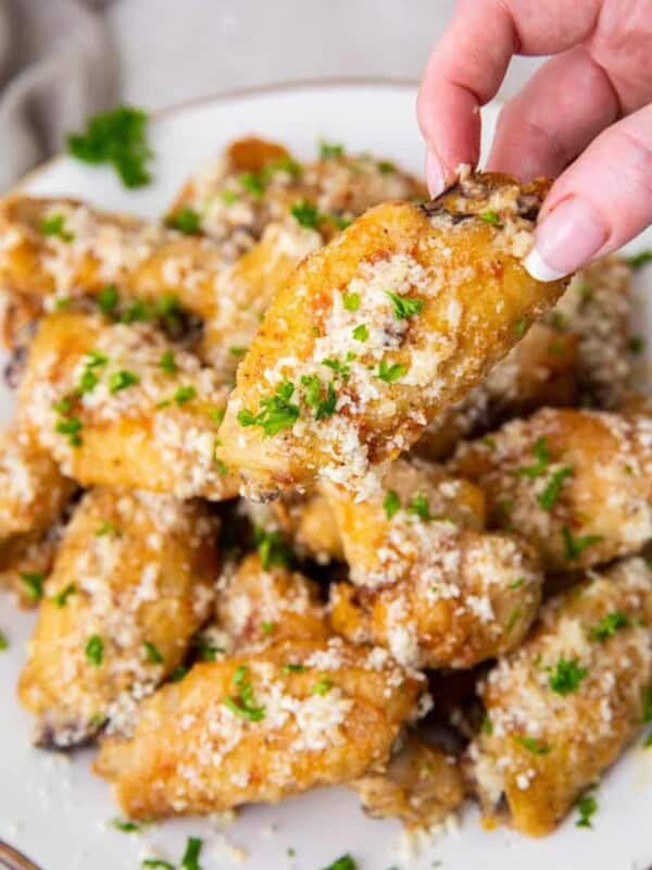 Hand reaching for one of many garlic parmesan wings on plate