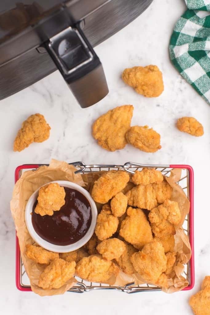plate with popcorn chicken and bbq sauce next to air fryer