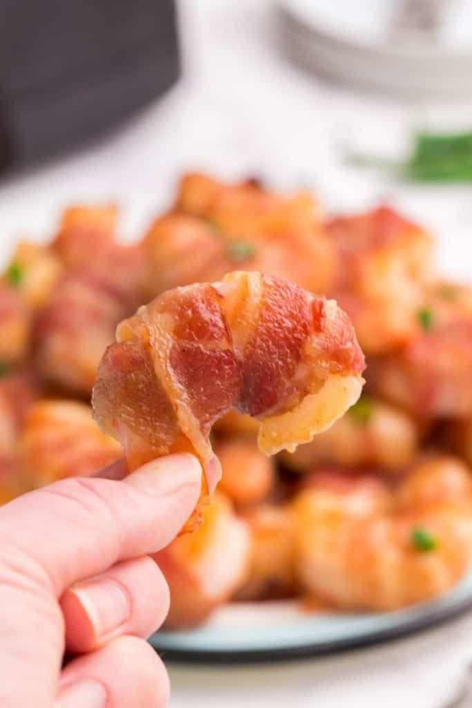 One bacon-wrapped shrimp in air fryer held up in front of full plate