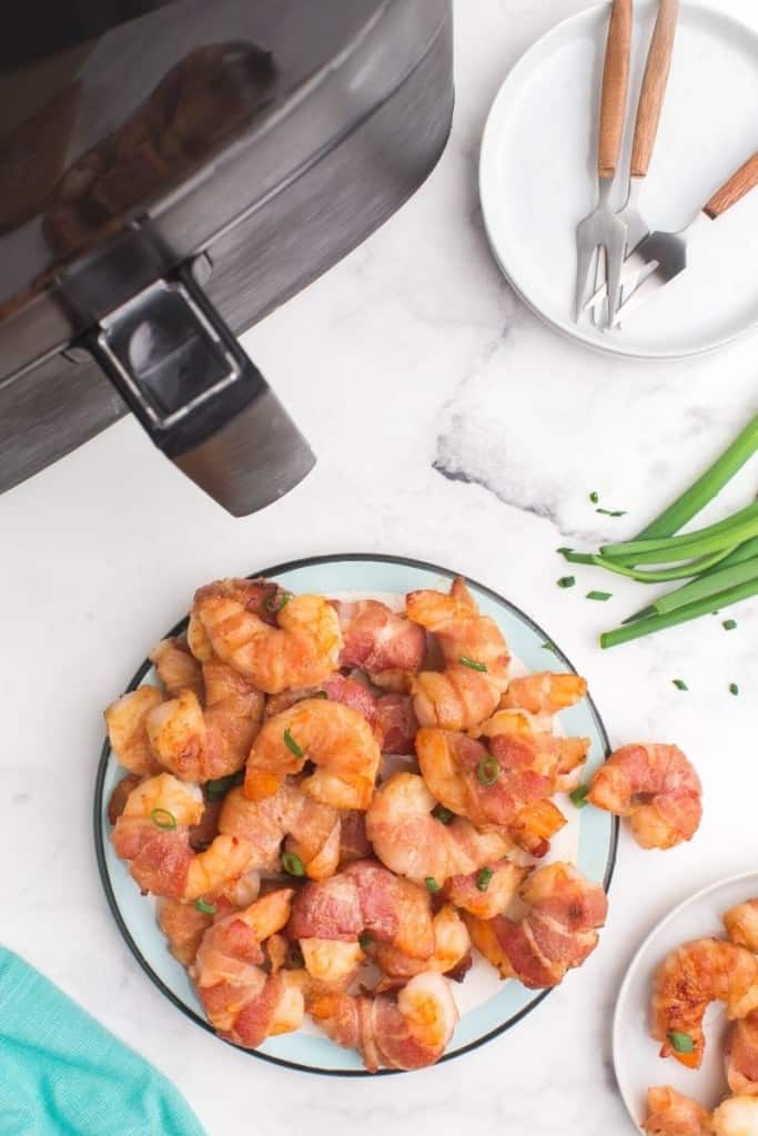 bacon-wrapped shrimp on plate next to air fryer