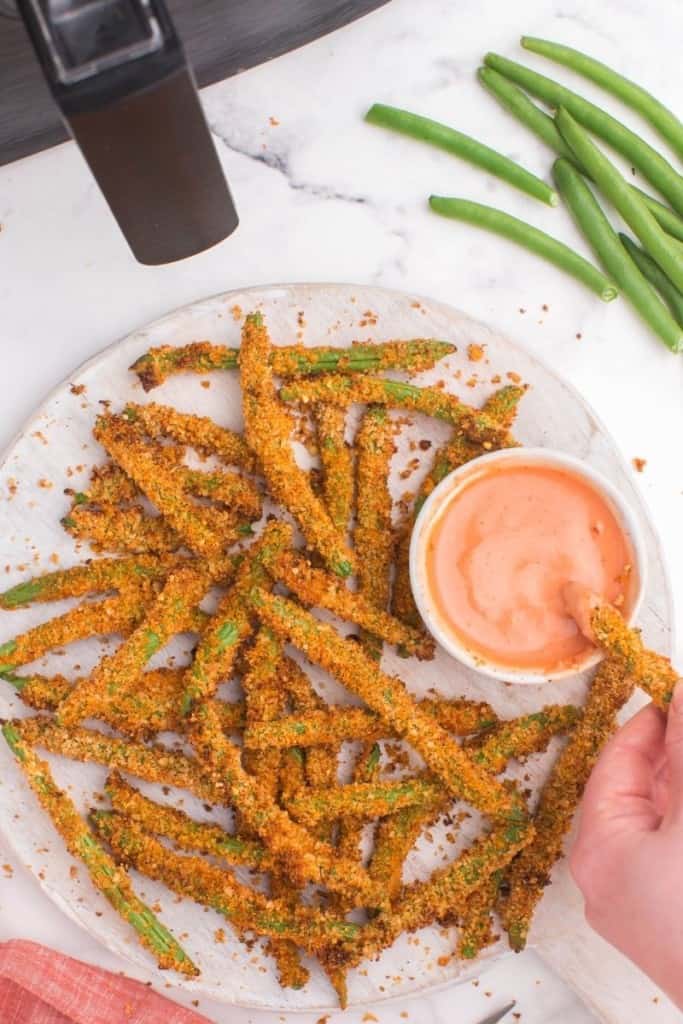 plate full of green bean fries with hand dipping a fry in sauce