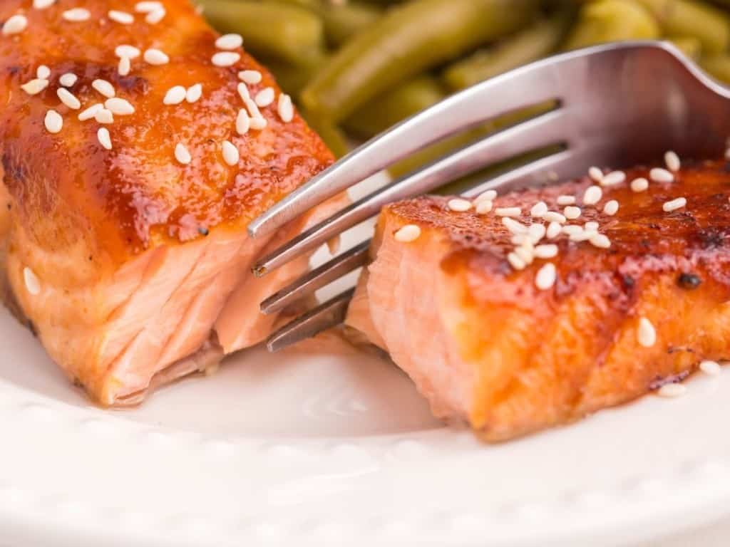 fork cutting air fryer teriyaki salmon filet in half