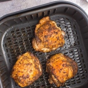 Fully cooked air fryer chicken thighs in an air fryer basket.