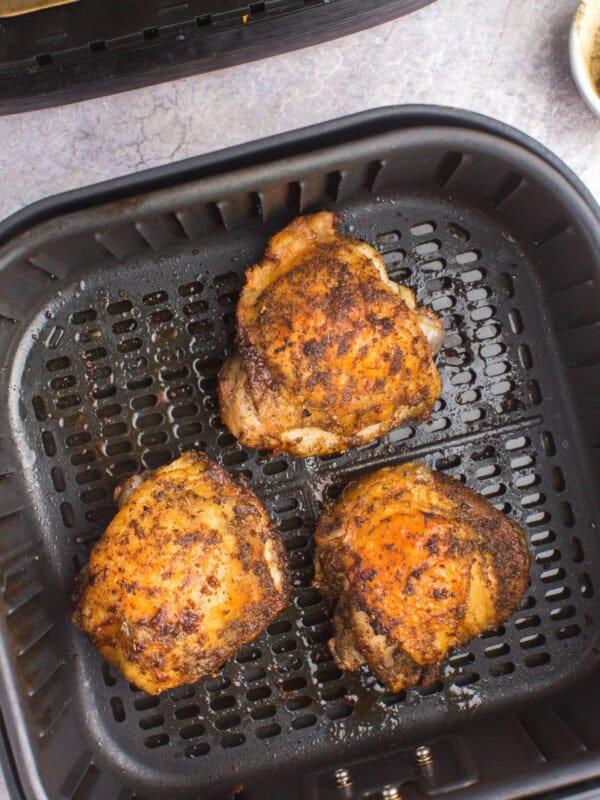Fully cooked air fryer chicken thighs in an air fryer basket.