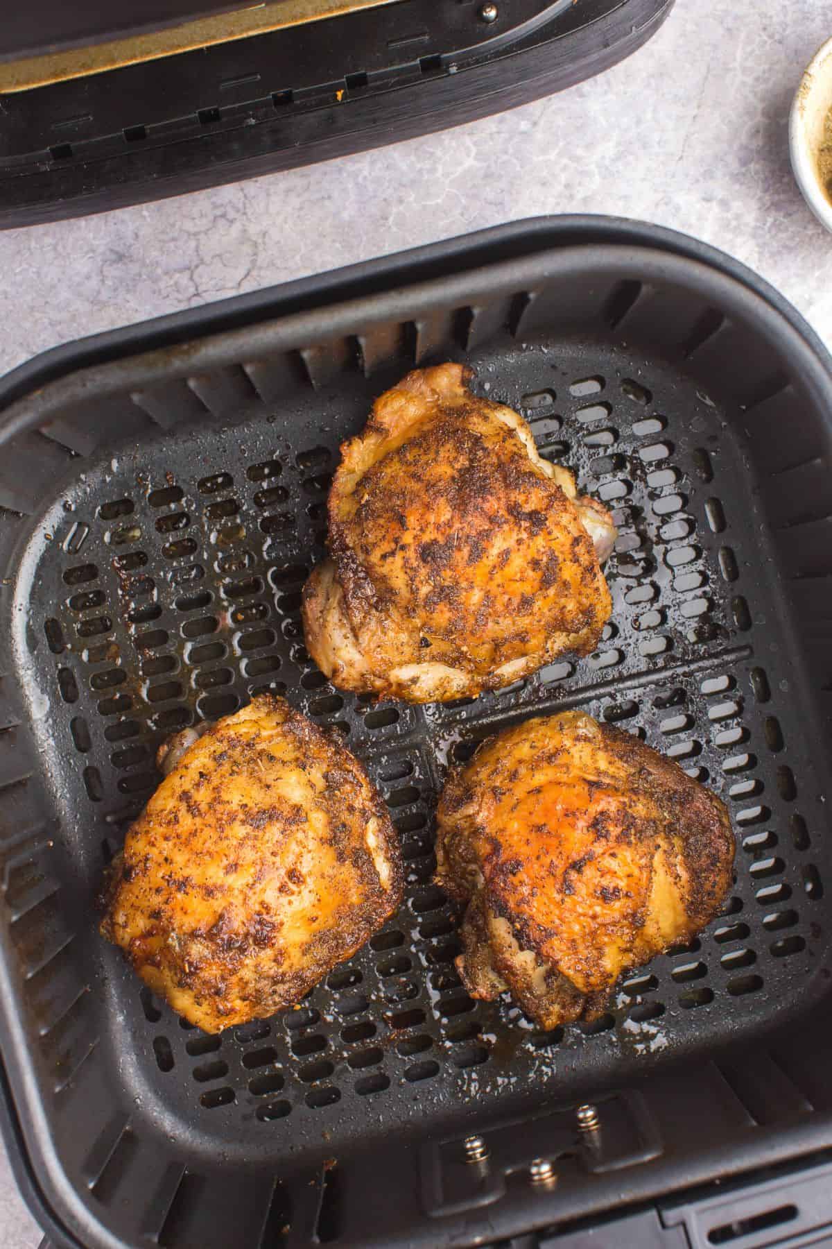 Fully cooked air fryer chicken thighs in an air fryer basket.