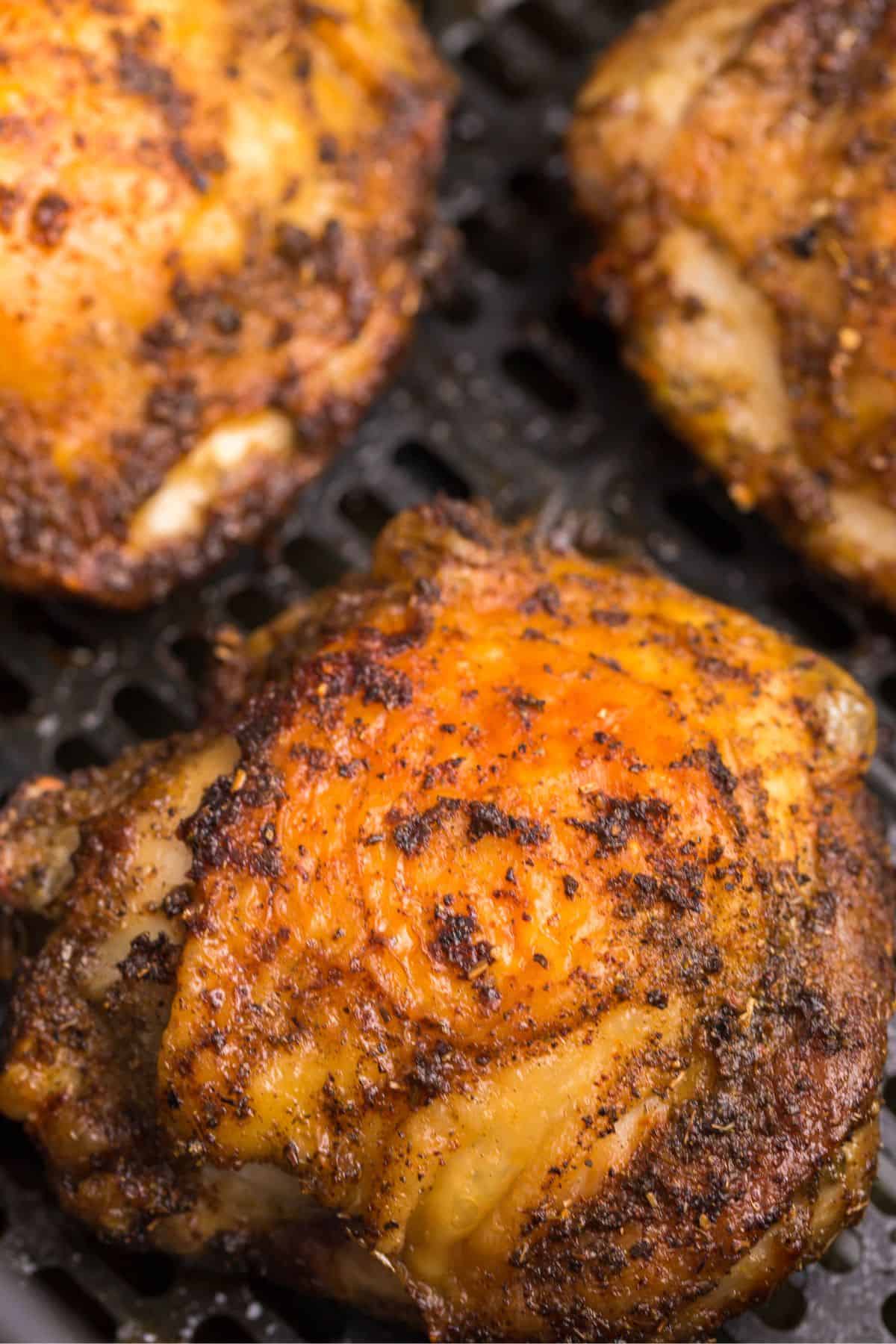 Close up of the chicken thighs while in an air fryer basket to see the golden brown skin on them.
