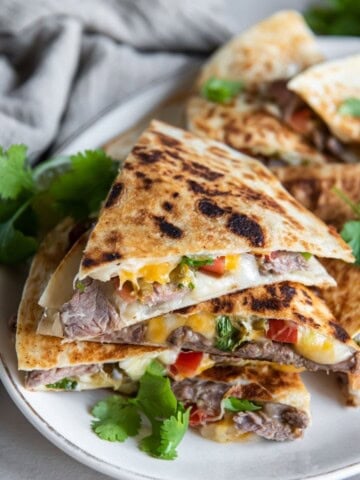 Carne asada quesadilla slices stacked on top of each other on a white plate.