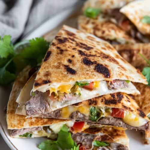 Carne asada quesadilla slices stacked on top of each other on a white plate.