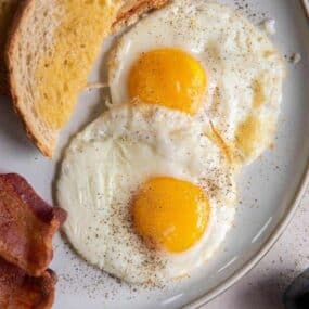 two air fryer fried eggs on plate with bread and bacon on side