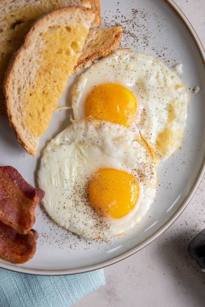 two air fryer fried eggs on plate with bread and bacon on side