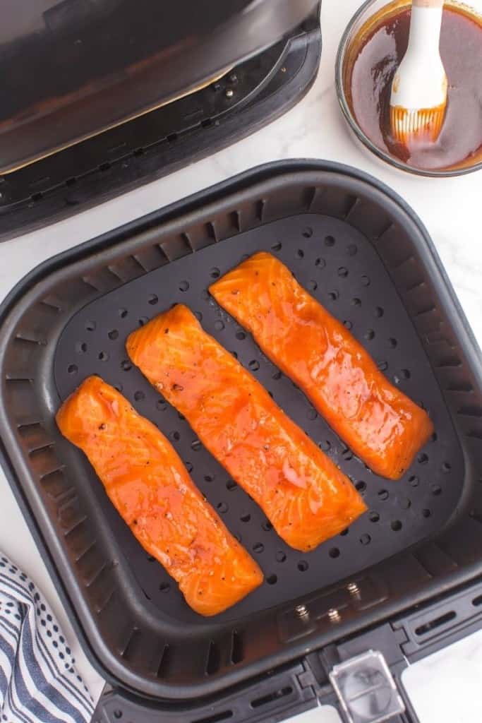 three salmon filets cooking in air fryer basket