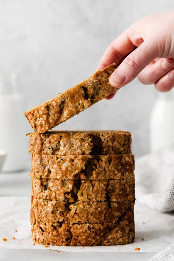 Zucchini bread with applesauce slices stacked on top of each other with a hand picking up the top slice.