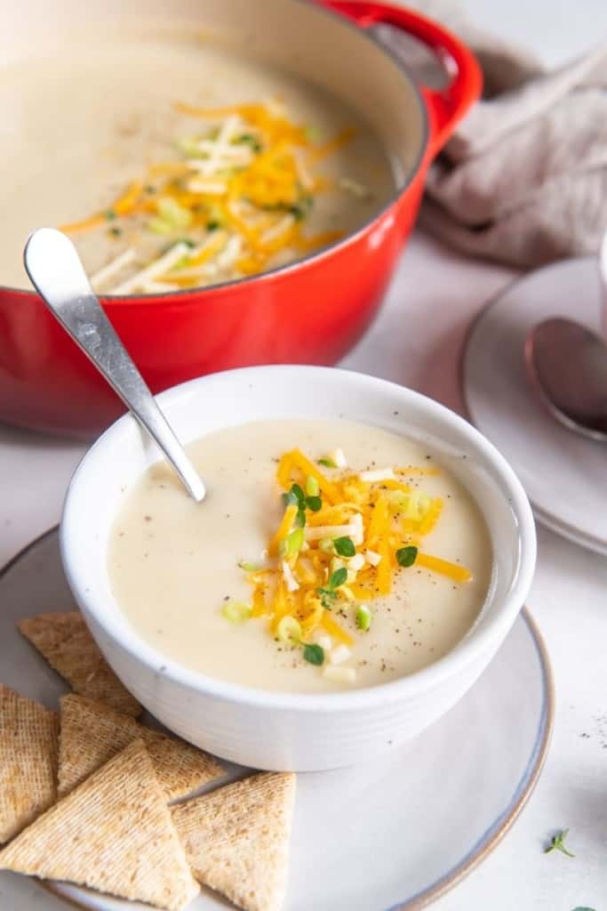 potato soup in white bowl with spoon and toppings sprinkled on