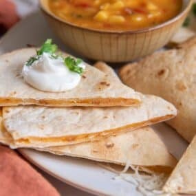 An air fryer quesadilla cut into slices with sour cream dolloped on top.