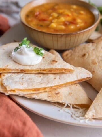 An air fryer quesadilla cut into slices with sour cream dolloped on top.