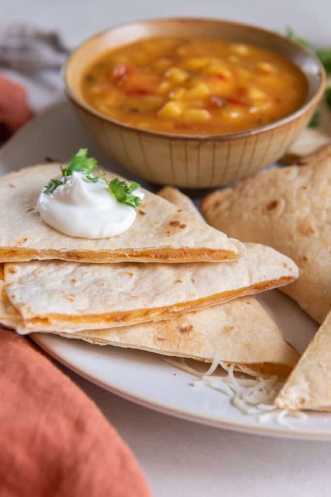 An air fryer quesadilla cut into slices with sour cream dolloped on top.