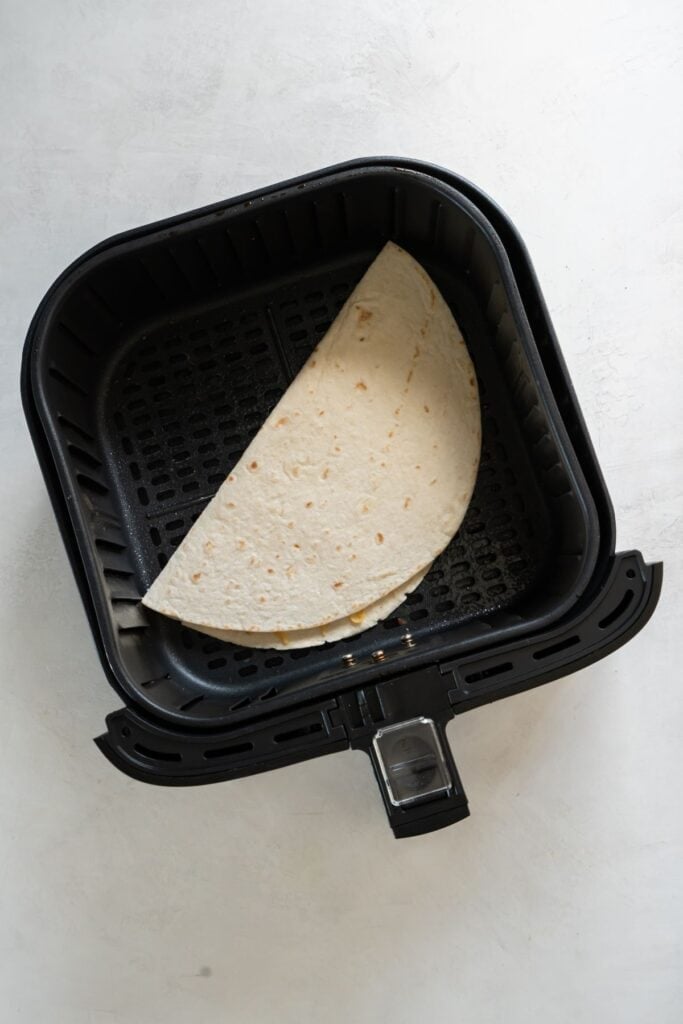 Quesadilla in an air fryer basket ready to be air fried.