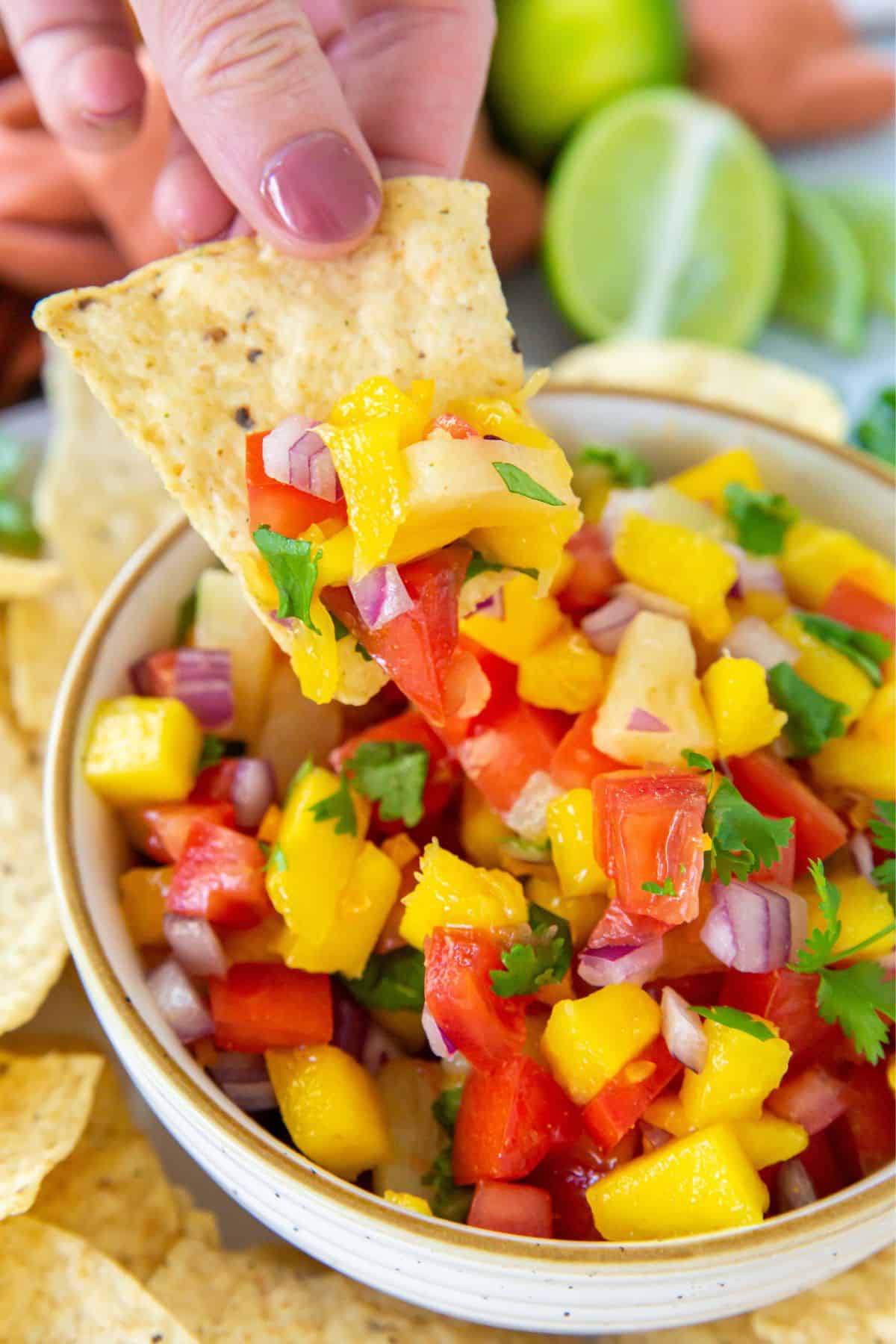 Mango habanero salsa in a serving dish with a tortilla chip being dipped into it.