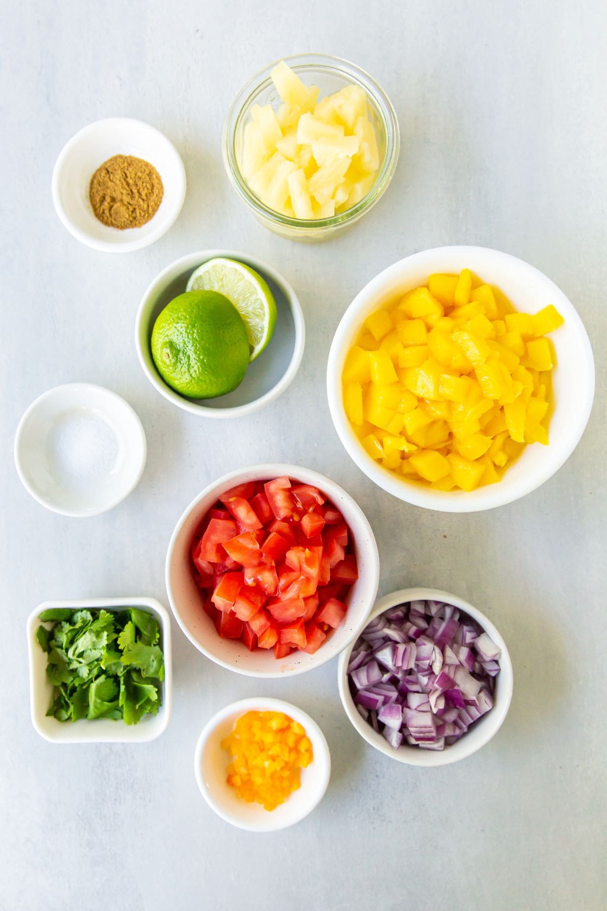 Ingredients needed to make mango habanero salsa: tomato, mango, habanero, pineapple, onion, cilantro, lime juice, salt, and cumin.